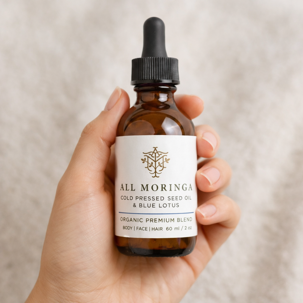 Hand holding a bottle of All Moringa cold pressed seed oil with blue lotus on a beige background