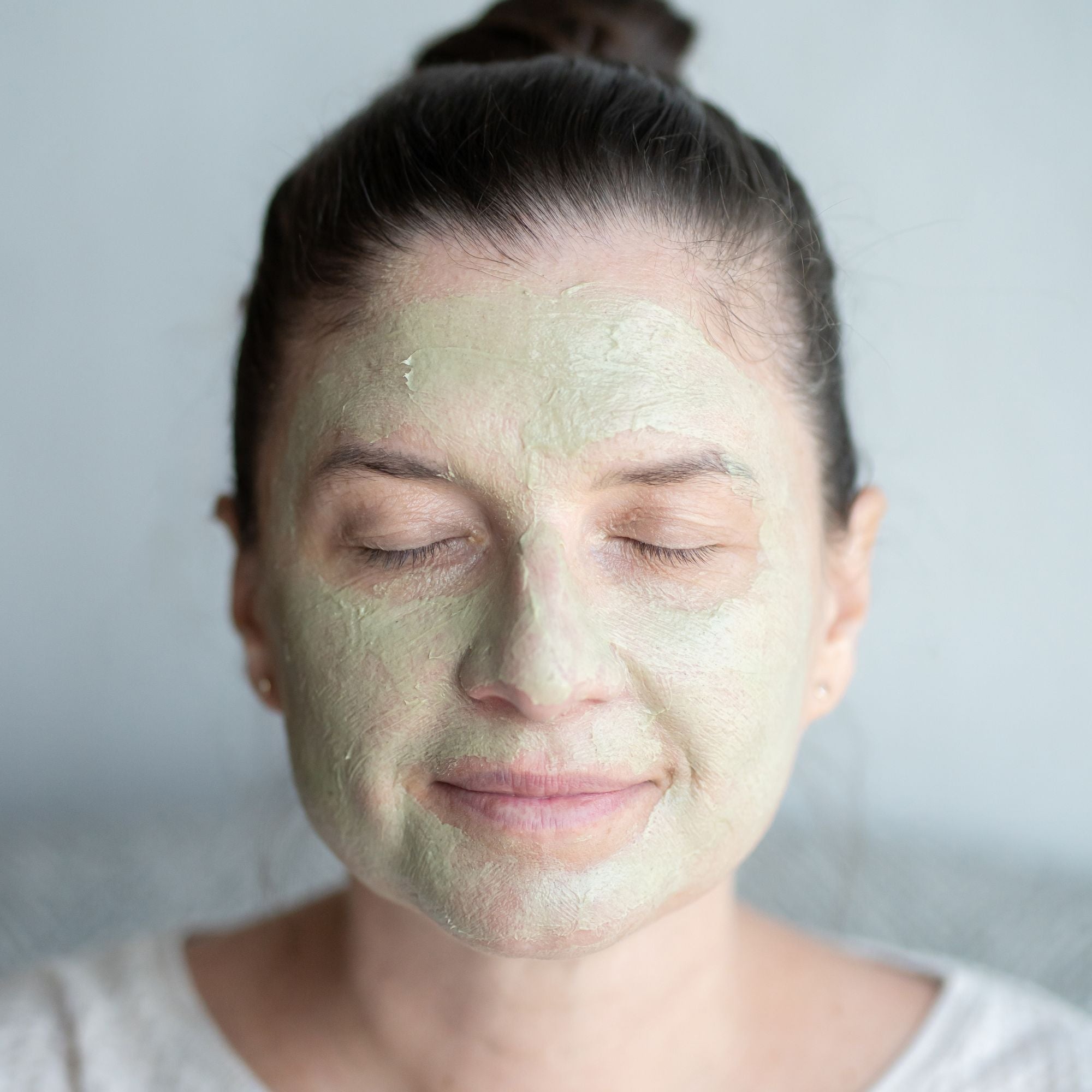 Woman applying a green moringa facial mask with a neutral background